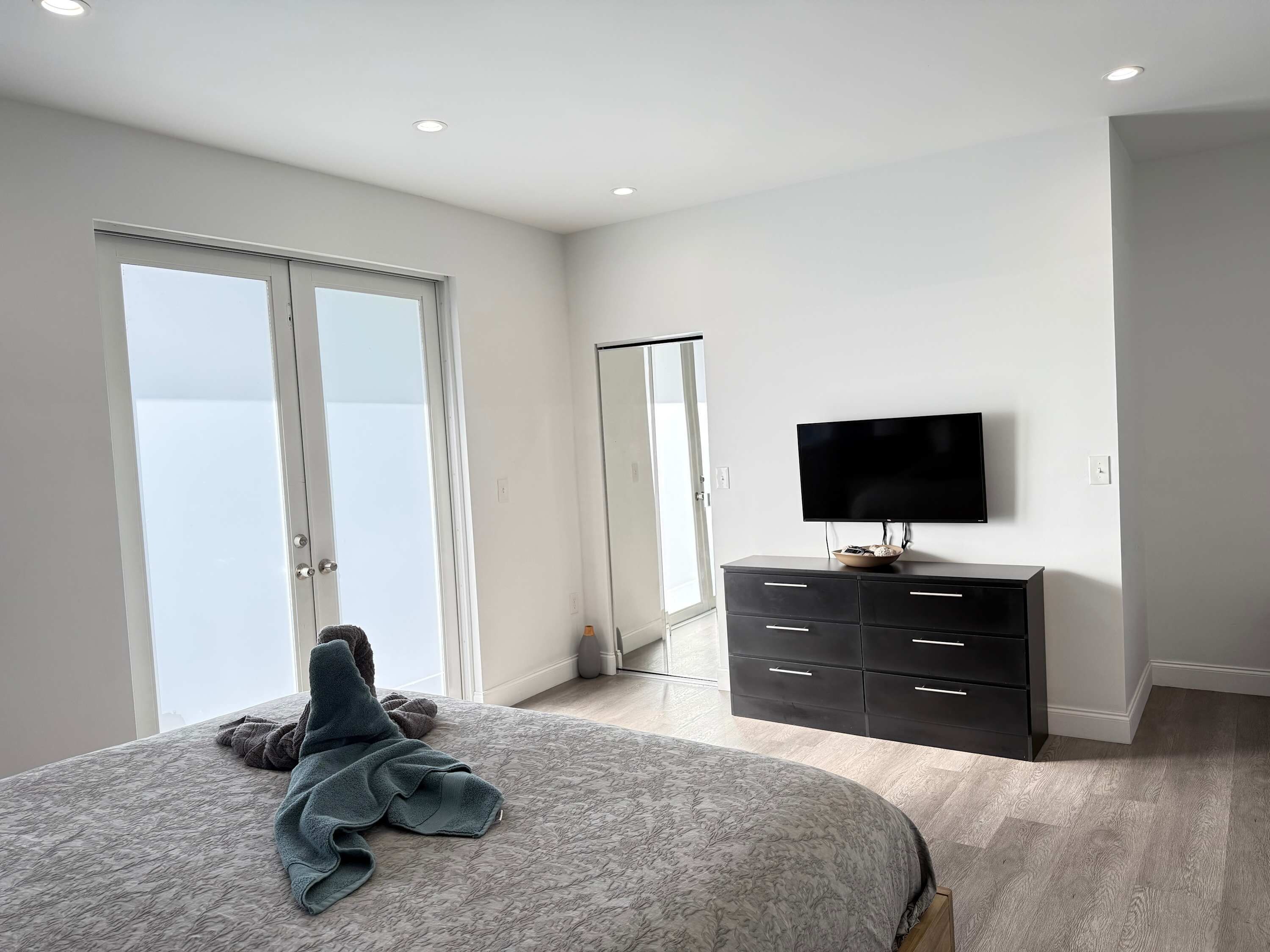 A bedroom with a bed, a dresser, a television, and a sliding glass door.