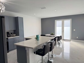 A modern kitchen with grey cabinets, a marble countertop, and a central island with bar stools. - Luxury 4BR Miami Villa With Hot Tub and Gazebo (Miami)