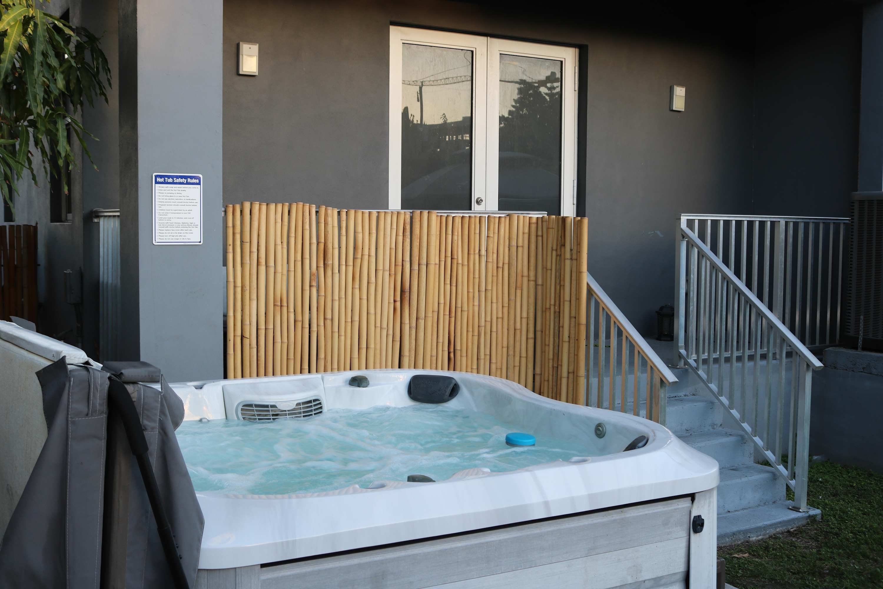 Un jacuzzi en un patio trasero con cerco de madera, barandilla de metal y un letrero con normas de seguridad.