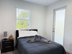 A bedroom with a bed, a nightstand, a window with blinds, and a door. - Luxury 4BR Miami Villa With Hot Tub and Gazebo (Miami)