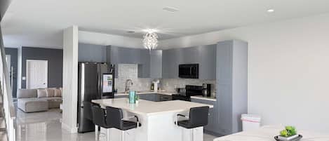 Una cocina moderna con armarios grises, una isla central con taburetes de bar, un refrigerador de acero inoxidable y un microondas.