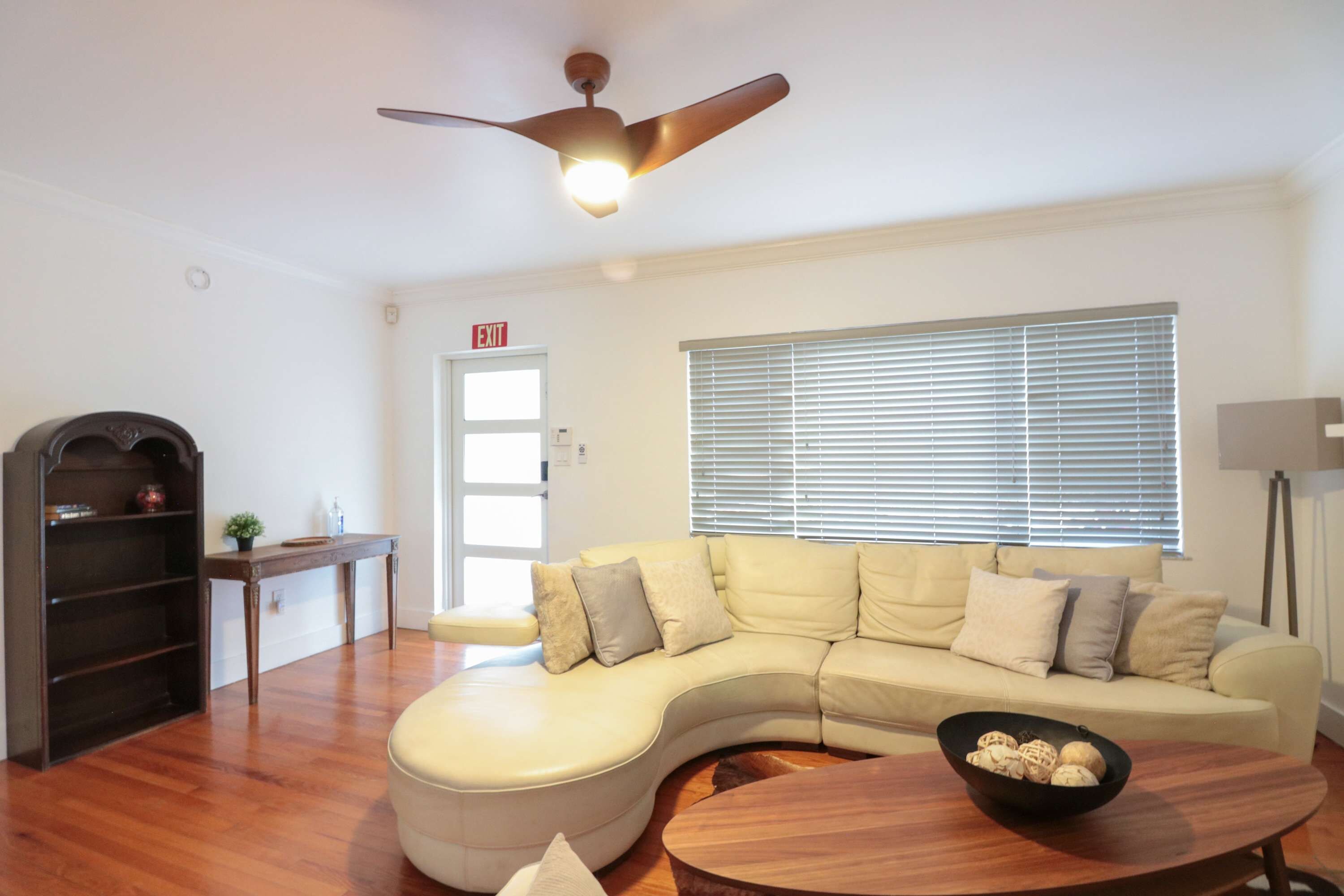 A living room with a curved sofa, a wooden coffee table, a ceiling fan, and a window with blinds.