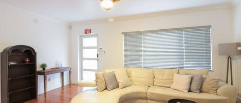A living room with a curved sofa, a wooden coffee table, a ceiling fan, and a window with blinds.