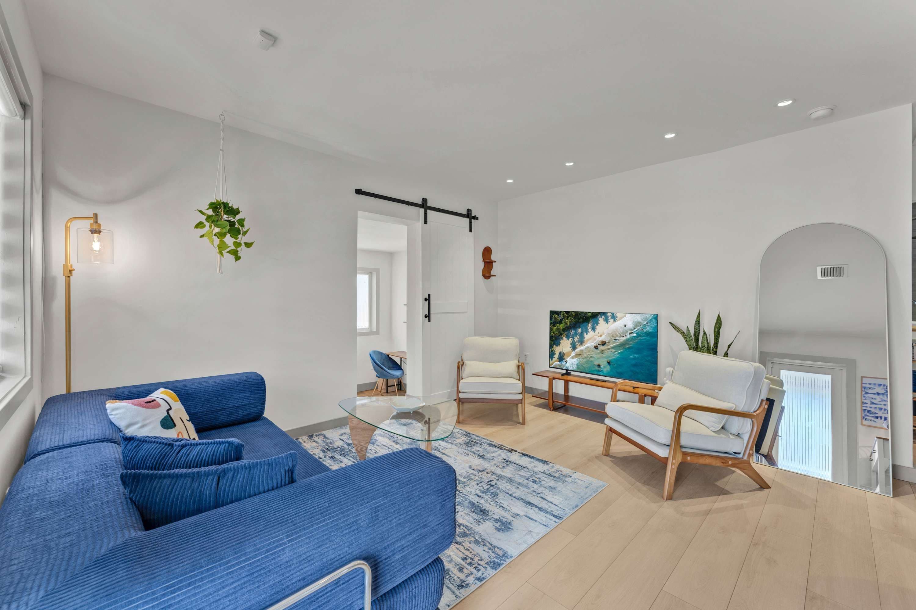 Un salon moderne avec un canapé bleu, une table basse en verre et un téléviseur posé sur un meuble en bois.