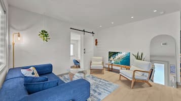 A modern living room with a blue sofa, a glass coffee table, and a TV on a wooden stand.