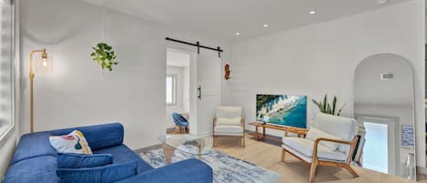 Un salon moderne avec un canapé bleu, une table basse en verre et un téléviseur posé sur un meuble en bois.