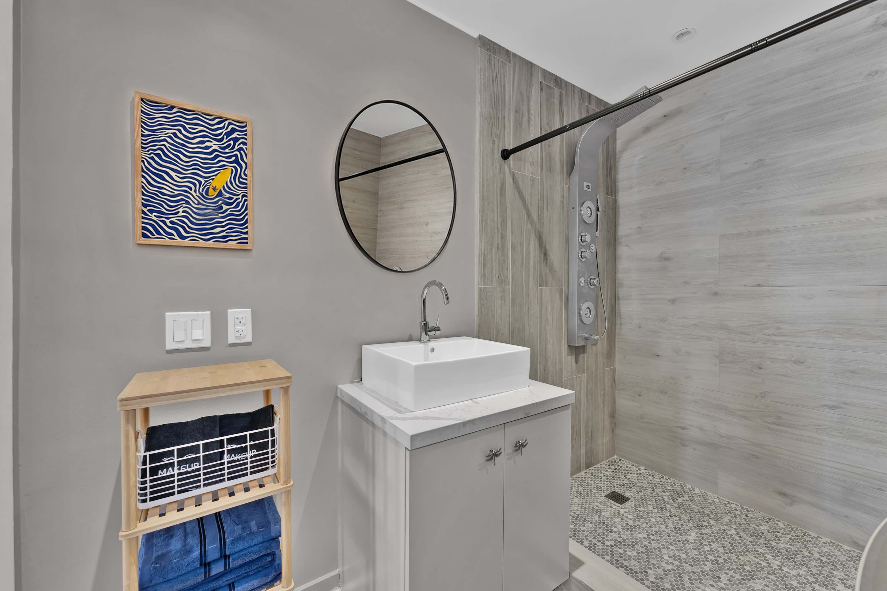 A modern bathroom with a shower, a sink, a mirror, and a towel rack.