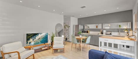 Un salon moderne doté d’un téléviseur à écran plat, d’un canapé, d’une table basse et d’un coin repas avec des chaises et une table.