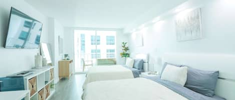 A modern hotel room with two beds, a TV, a desk, and a view of the city.