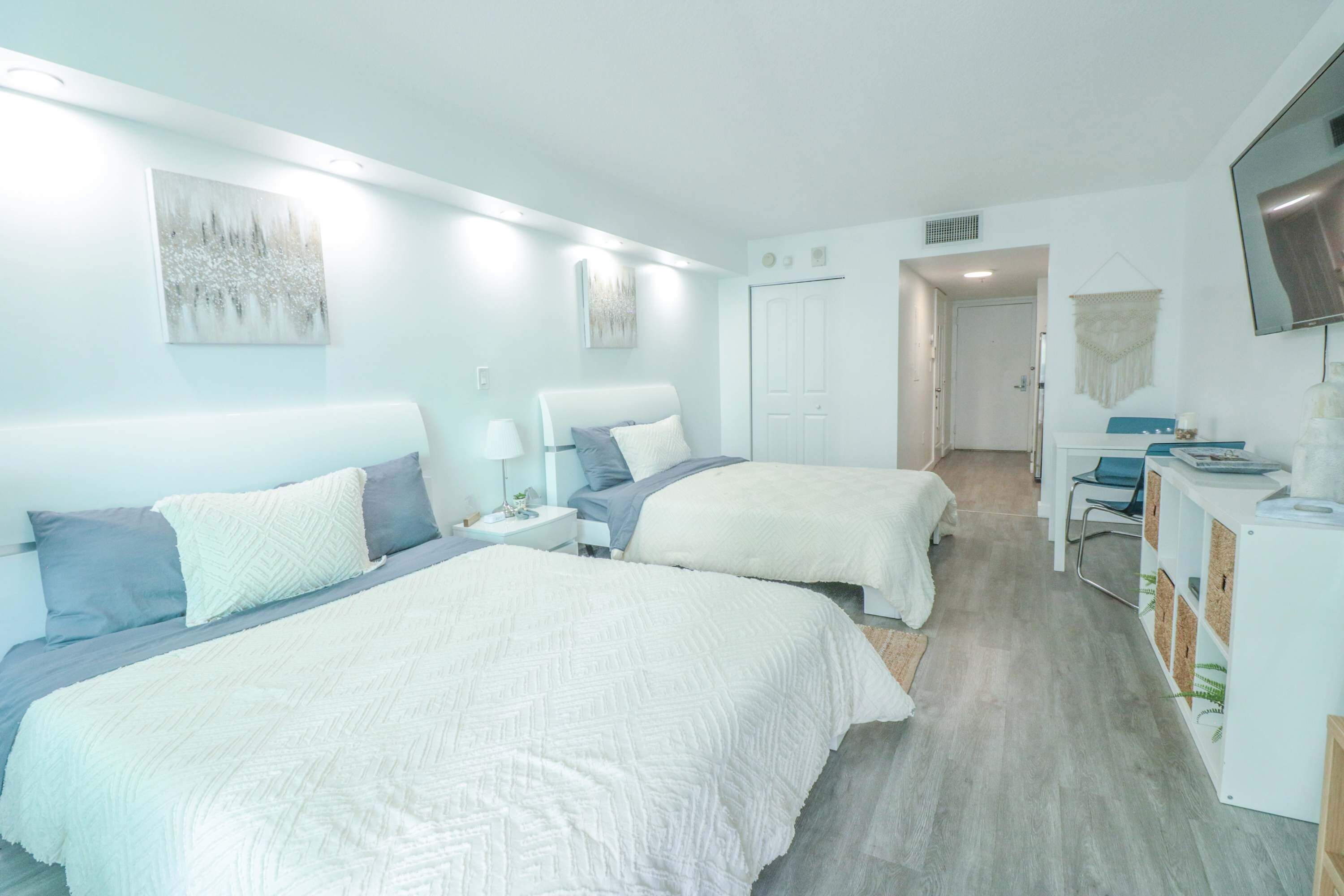 A hotel room with two beds, a desk, a television, and artwork on the walls.