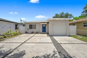 A residential house with a front garage, a blue door, and a driveway leading to the entrance. - Modern 4BR Villa Near Hollywood Beach FTL (Hollywood)