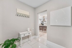 A hallway with a white console table, a plant, a wall-mounted coat rack, and a doorway leading to a kitchen area. - Modern 4BR Villa Near Hollywood Beach FTL (Hollywood)
