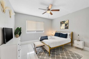 A bedroom with a bed, bedside table, lamp, ceiling fan, window with blinds, and a wall-mounted TV. - Modern 4BR Villa Near Hollywood Beach FTL (Hollywood)
