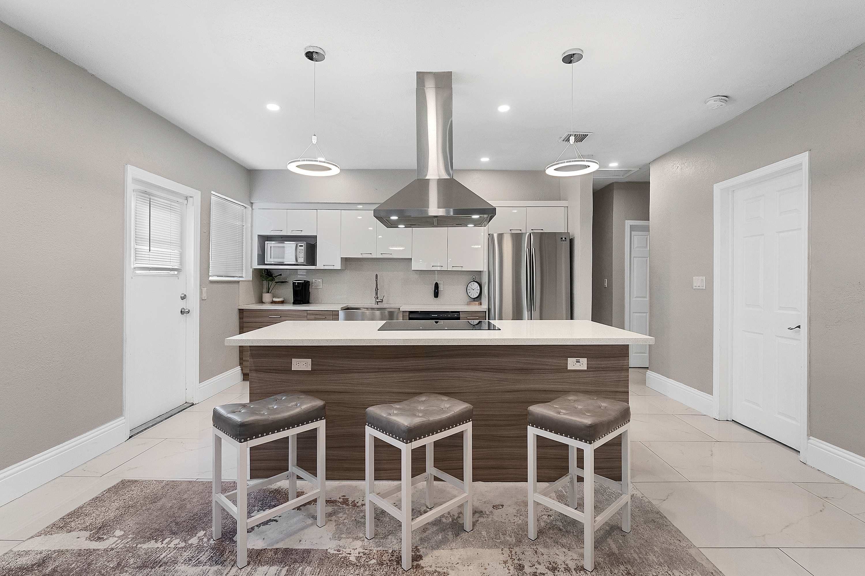A modern kitchen with a central island, stainless steel appliances, and bar stools.