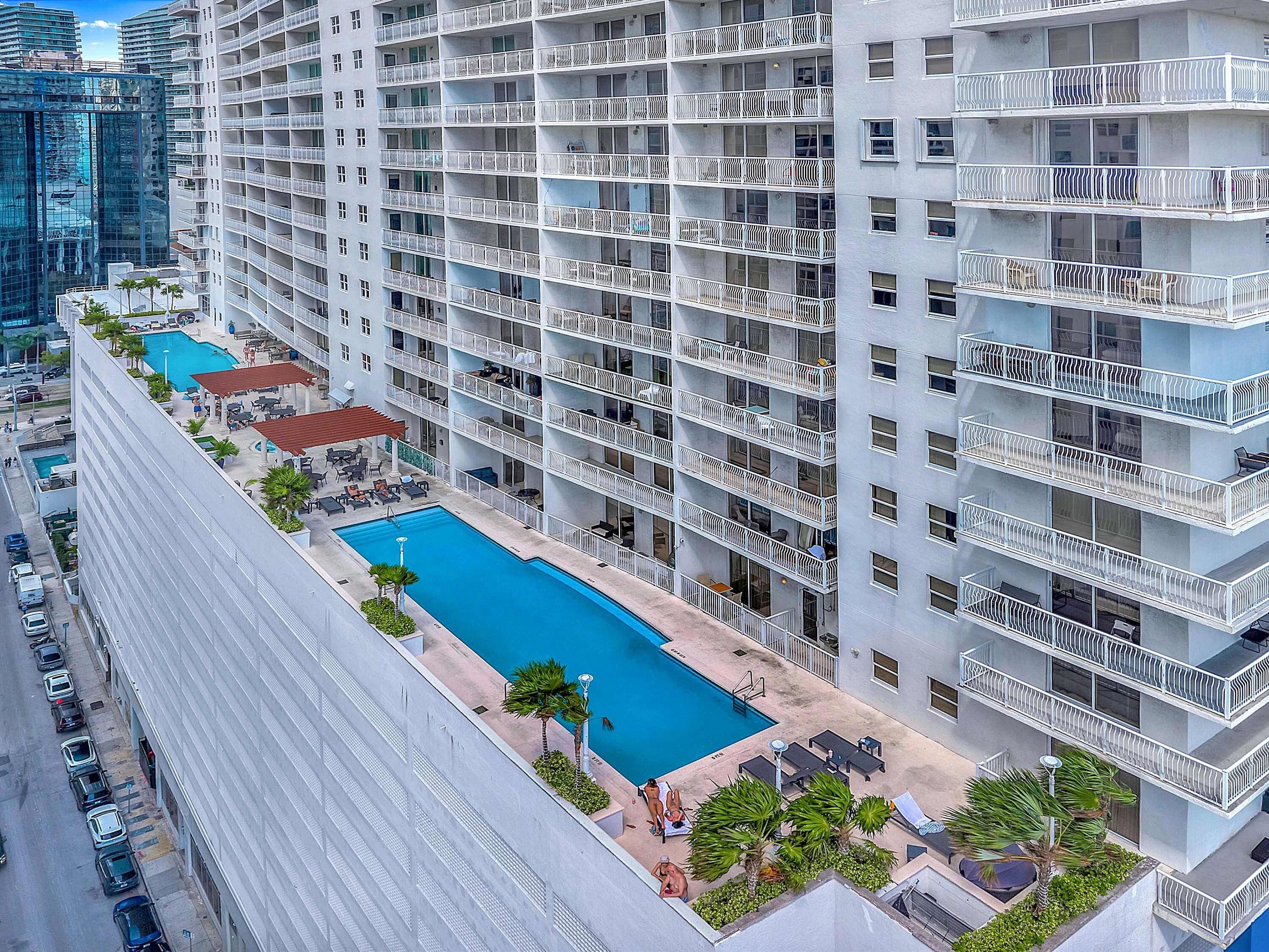 A high-rise building with multiple balconies, a swimming pool, and outdoor seating areas.
