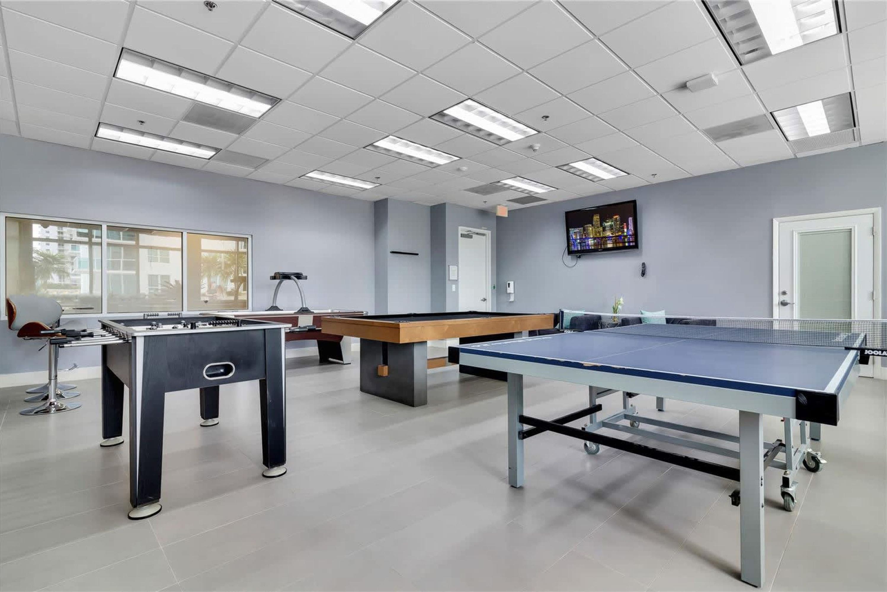 A recreational room with a foosball table, pool table, and ping pong table.
