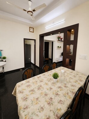 A dining area with a table covered in a floral tablecloth, surrounded by chairs.