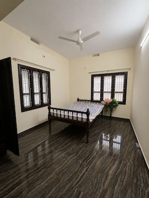 A room with a bed, two windows with bars, a ceiling fan, and a dark floor.