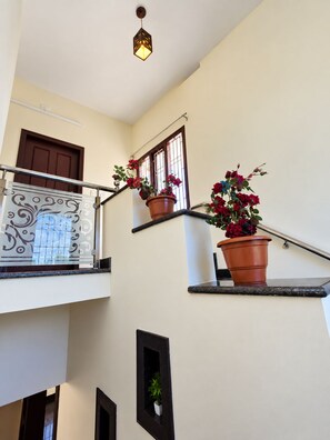 A staircase with a railing, a potted plant, and a decorative light fixture. - Entire 3BHK Homestay Near Beach For Groups & Family. (Mulki)