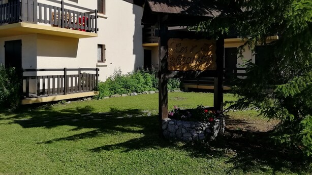 A residential building with balconies, a stone wall, and a pergola with flowers. - Vrbo Property (Risoul)
