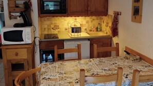 A compact kitchen with wooden cabinets, a microwave, a sink, and a dining table with chairs. - Vrbo Property (Risoul)