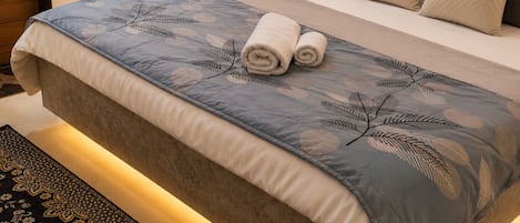 A neatly made bed with a patterned bedspread, a headboard, and a bedside table with a lamp.