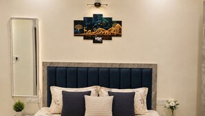 Een slaapkamer met een bed, een hoofdbord, een kunstwerk aan de muur, een nachtkastje, een spiegel en een vaas met bloemen.