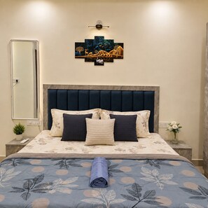 Ein Schlafzimmer mit einem Bett, einem Kopfteil, einem Wandbild, einem Nachttisch, einem Spiegel und einer Vase mit Blumen.