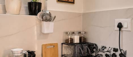Una cocina con cafetera, sartén, tabla de cortar y especiero.