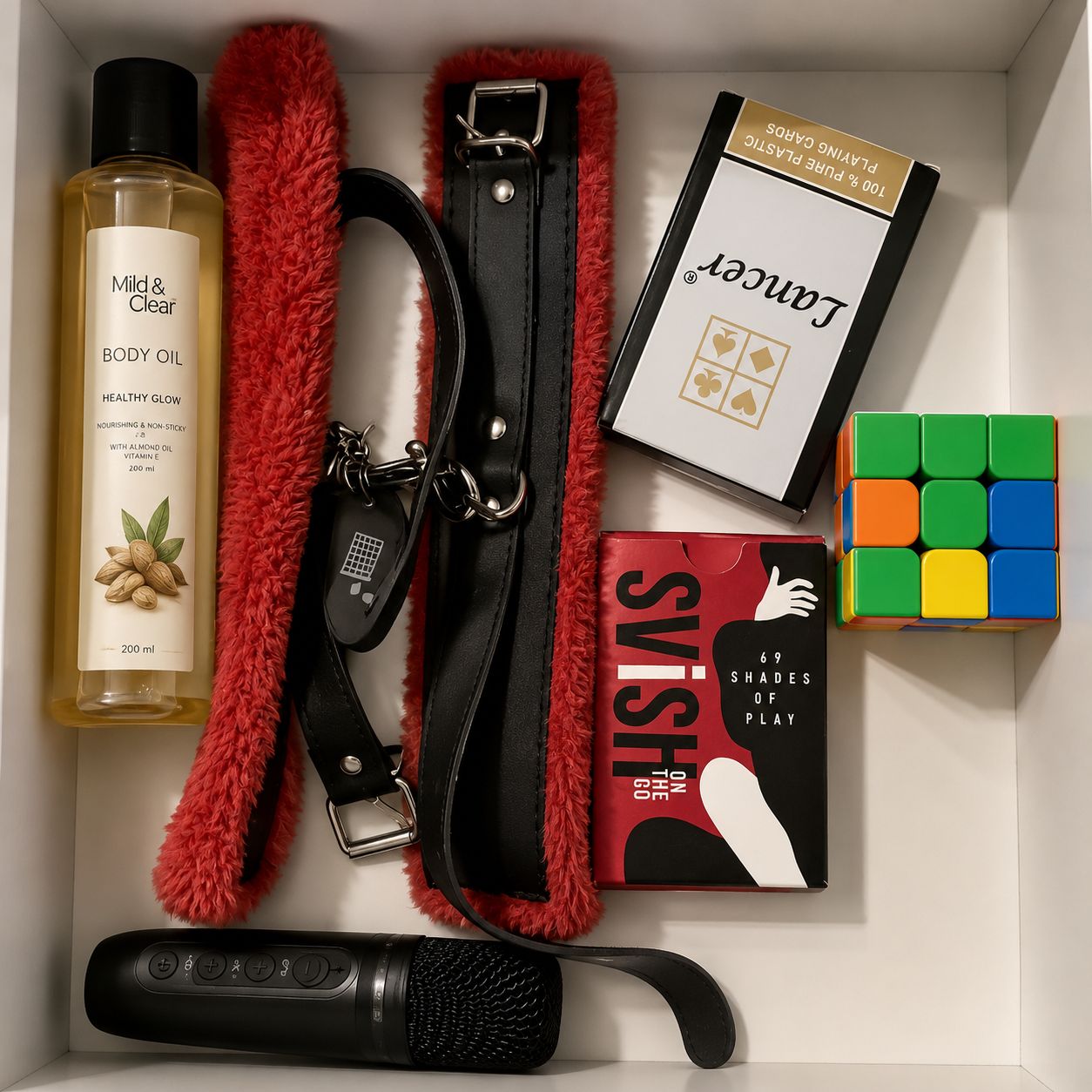 A neatly organized drawer with a bottle of body oil, a red fluffy item, a black strap, a book, a Rubik's cube, and a remote control.