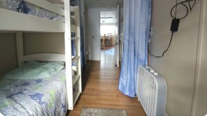 Une chambre avec un lit superposé, un radiateur, un rideau et un couloir menant à un coin repas.