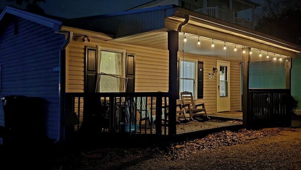 Une maison à deux étages avec un porche, un espace extérieur couvert agrémenté de guirlandes lumineuses et un garage dont la porte est visible.
