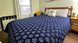 Une chambre à coucher avec un lit, une fenêtre avec des rideaux, une table de chevet et un panneau décoratif au mur.