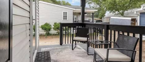 A covered porch with a black railing, two chairs, and a patterned rug.