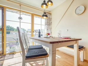 A dining area with a wooden table, chairs, and a view through large windows. - 2.6/t3 Holiday Home Park \"freesenbruch\" (Zingst)
