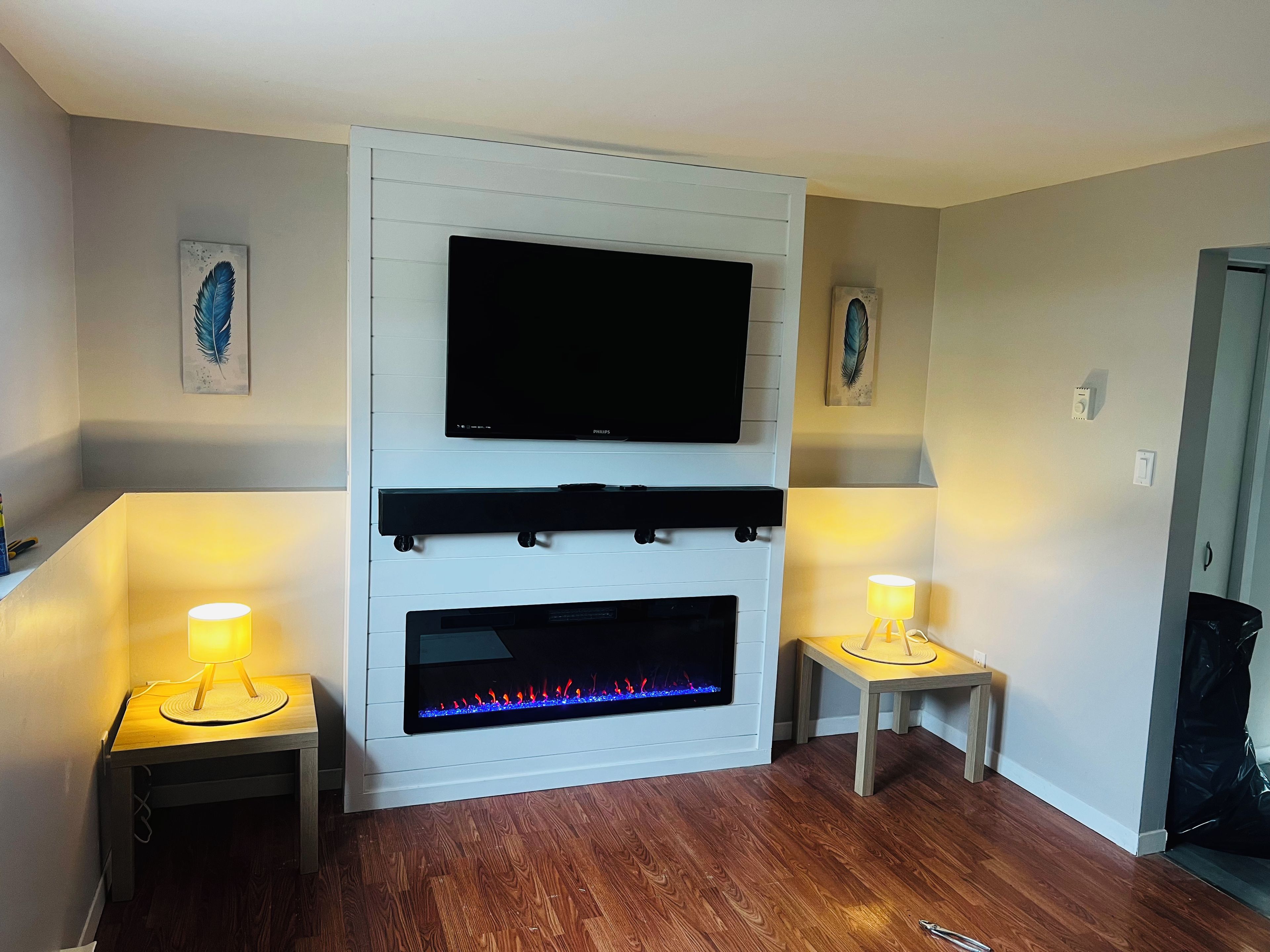 A living room with a flat-screen TV mounted above a fireplace, flanked by two small tables with lamps.