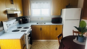 A kitchen with wooden cabinets, a white stove, a microwave, and a sink. - Cozy 1 Bdr Apartment (Mount Pearl)