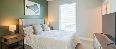 A bedroom with a bed, bedside lamps, a dresser, a window with blinds, and a painting on the wall.