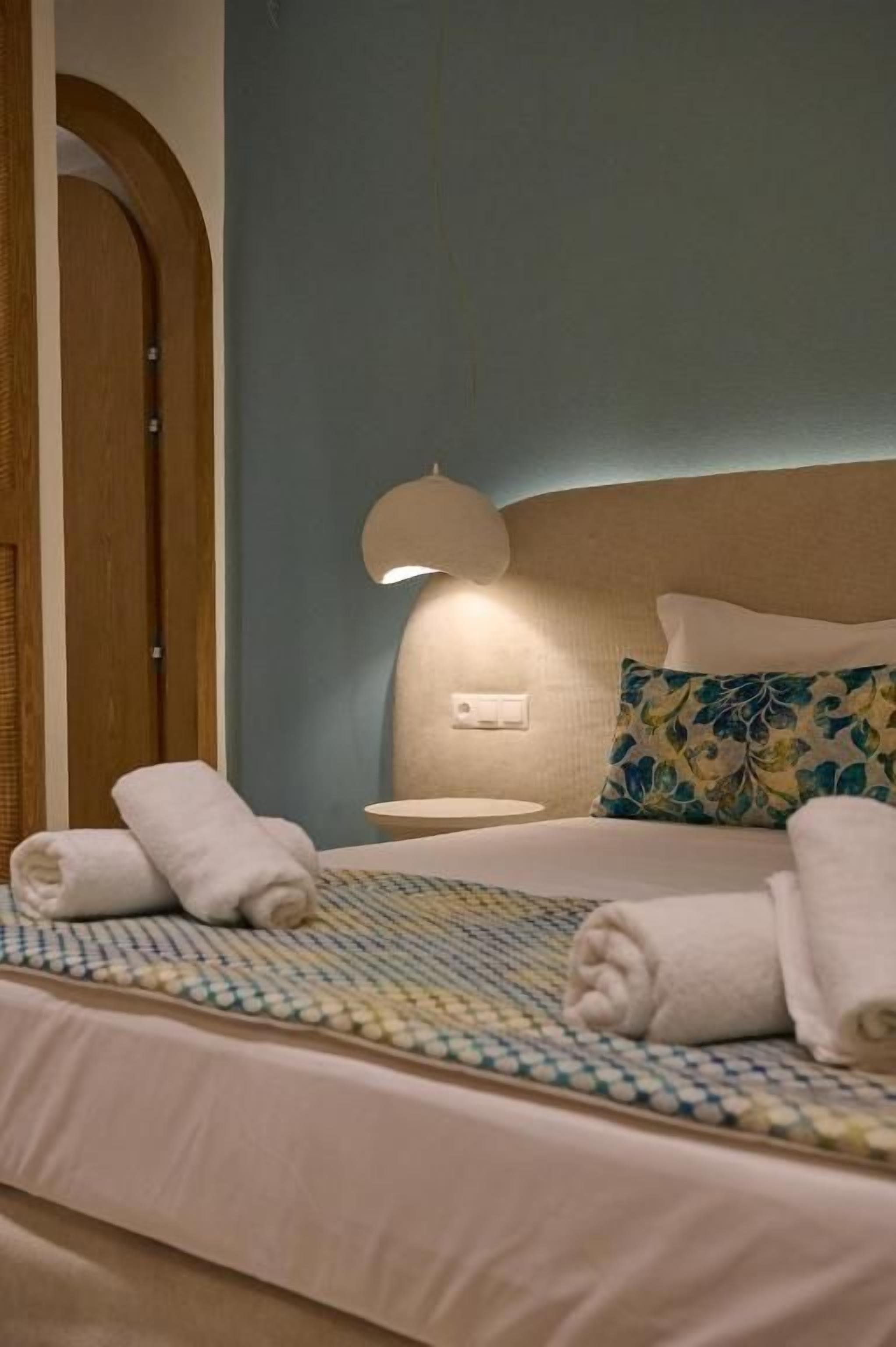 A neatly made bed with rolled towels, a bedside lamp, and a floral pillow.