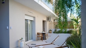 A modern outdoor seating area with a table and chairs, a sun lounger, and a small side table with a cup and saucer. - Perea Fiore Suites (Perea)