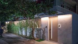 A modern building with a well-lit entrance, a small garden area, and a pathway leading to the entrance. - Perea Fiore Suites (Perea)