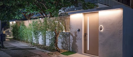 Un edificio moderno con una entrada bien iluminada, un pequeño jardín y un camino que lleva a la entrada.