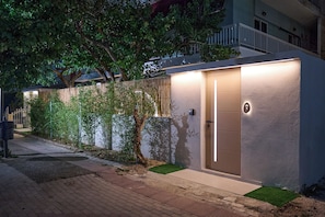 Un edificio moderno con una entrada bien iluminada, un pequeño jardín y un camino que lleva a la entrada.