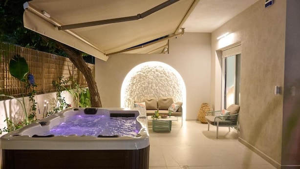 A hot tub in a covered outdoor area with a seating arrangement and a wall-mounted light fixture. - Perea Fiore Suites (Perea)