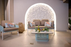 Un área lounge moderna con sofá, sillón y mesa de centro, que destaca por una pared con textura y una gran lámpara circular.