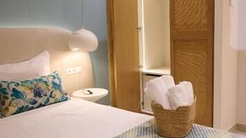 Habitación de hotel con cama, mesita de noche, armario de madera y una cesta con toallas.