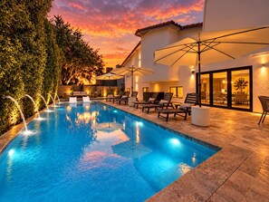 Ein Swimmingpool mit Liegestühlen und Sonnenschirmen, umgeben von einem Gebäude mit großen Fenstern.
