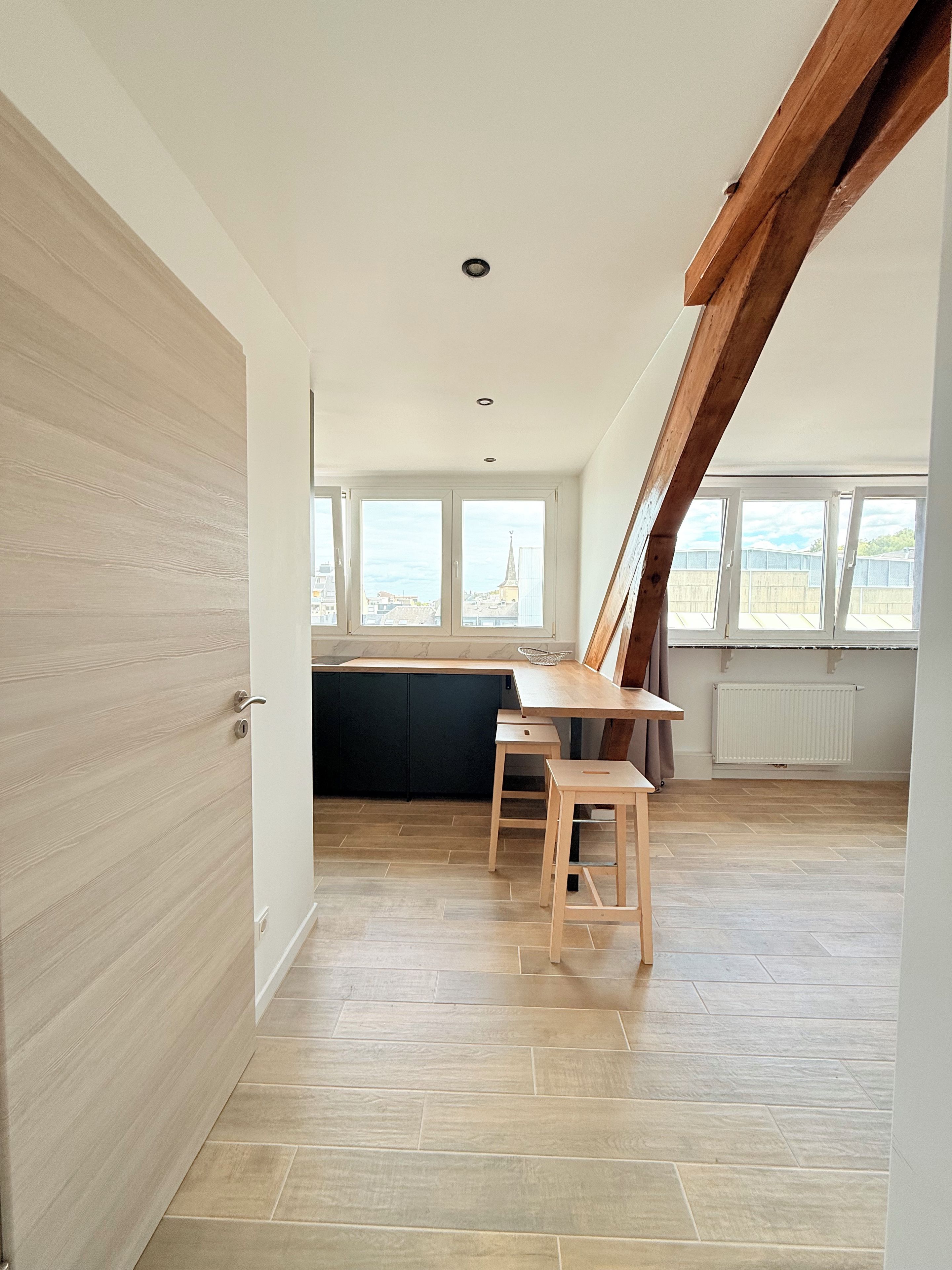 A modern kitchen with a wooden countertop, a black cabinet, and a window overlooking a cityscape.