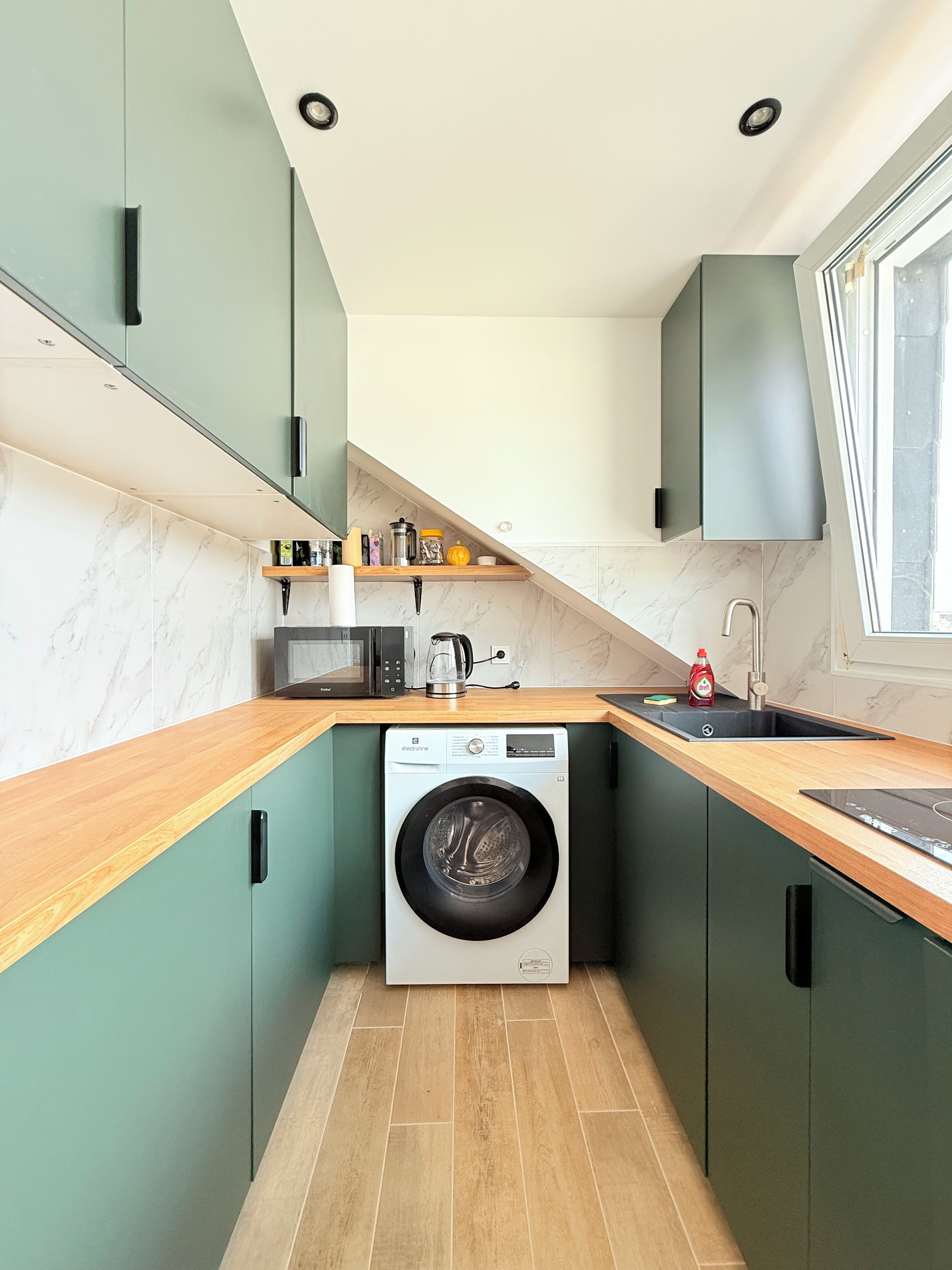Una cocina compacta con lavadora integrada, un lavamanos y una ventana.