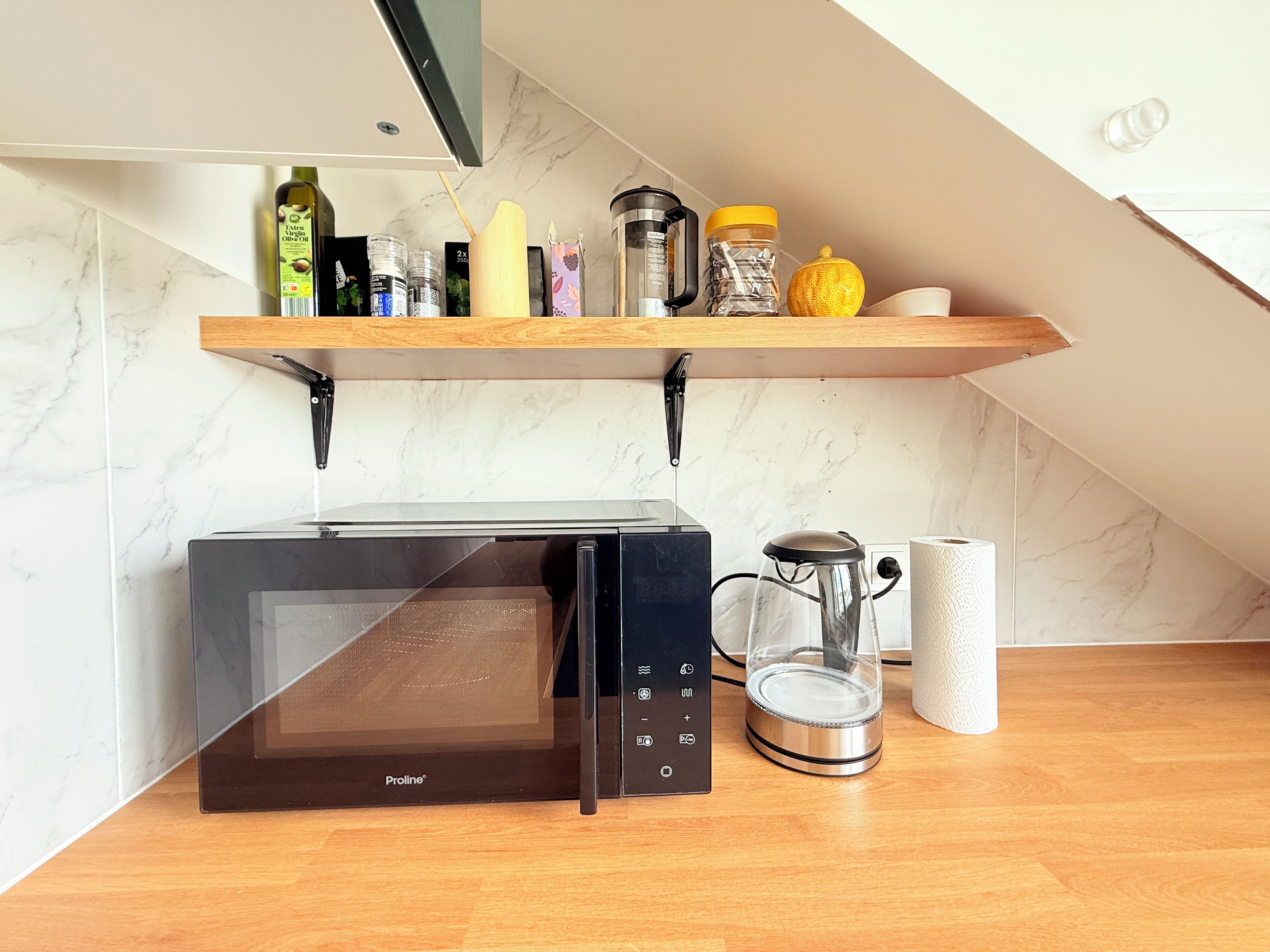 A kitchen with a microwave, a coffee maker, and a shelf with various items.